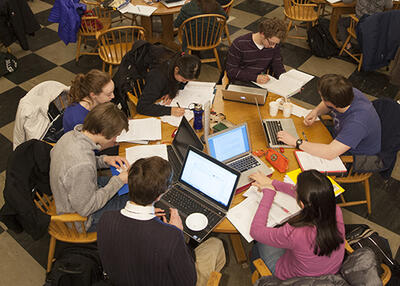 students gathered in dining hall working on laptops while sitting around a circular table
