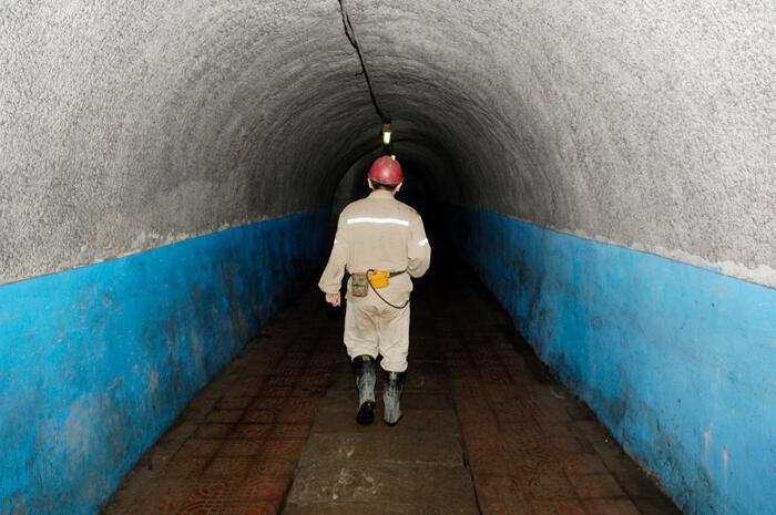 Back of coal miner in gear walking down a dark tunnel