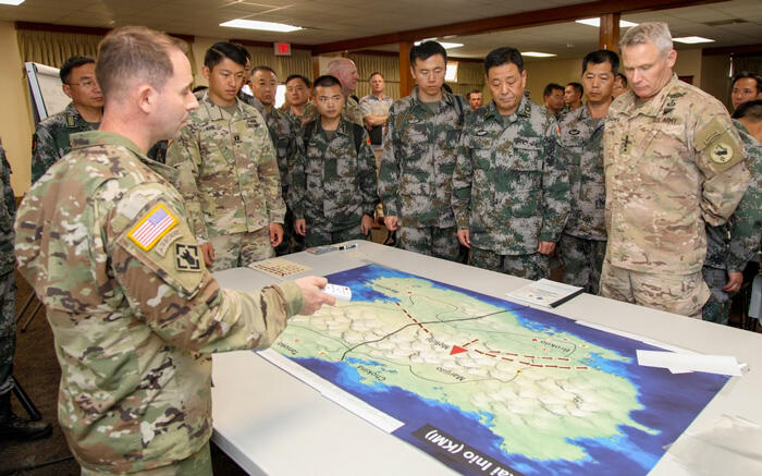 US and PLA military members gathered around a table looking at a map of China