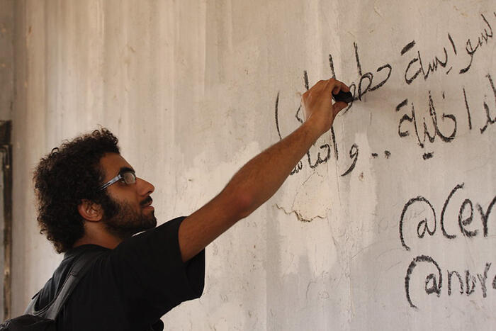 Profile of a man writing in Arabic on a wall