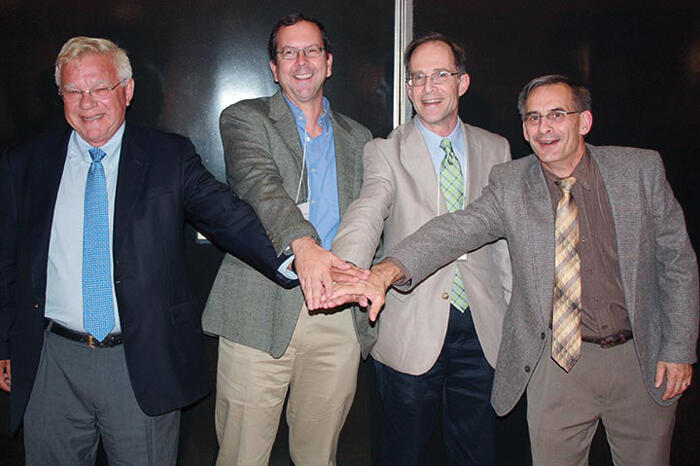 Group photo of the past 4 Harvard Academy Executive Officers reaching their hands into the middle