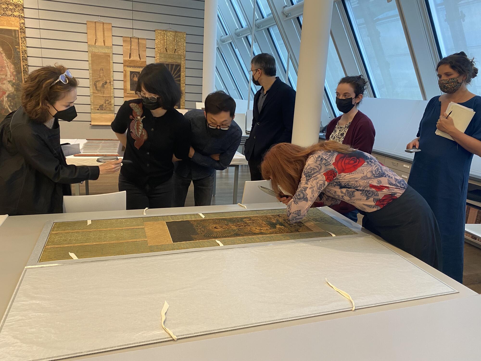 Several people look closely at a textile image on a table