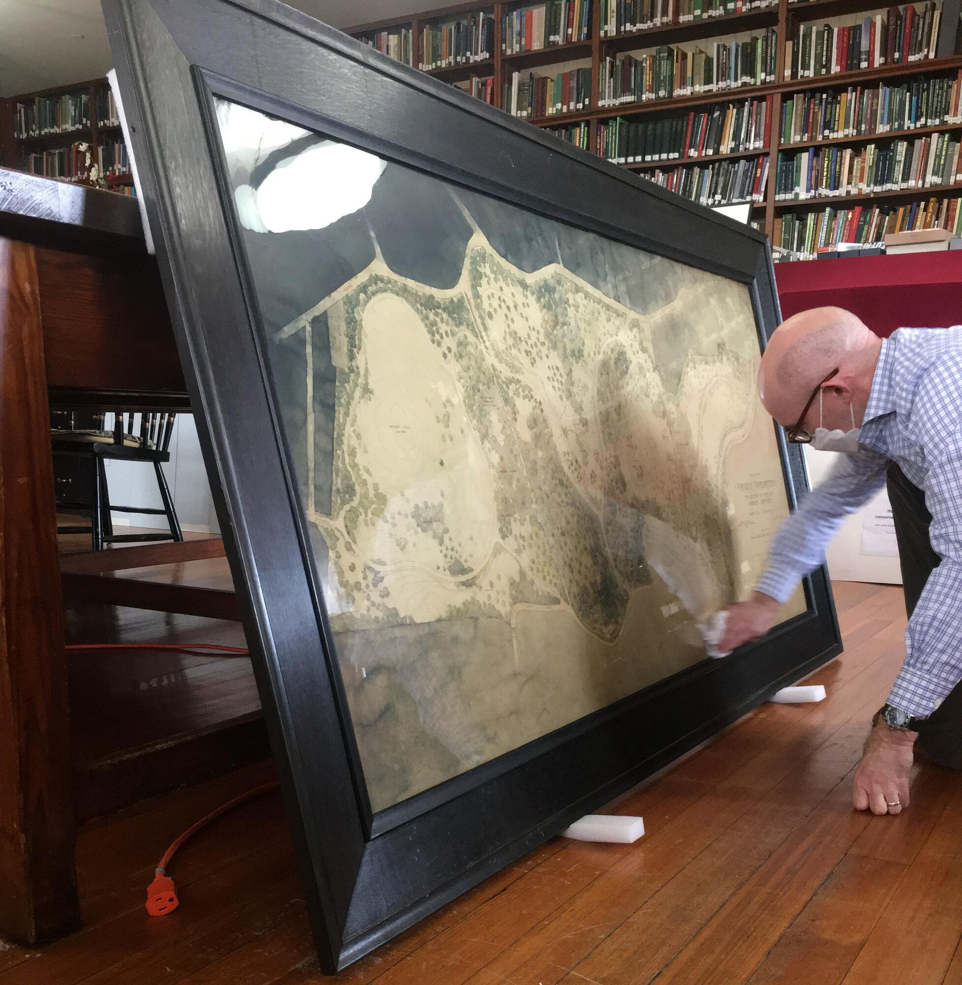 A man cleaning the glass on a large, framed map.