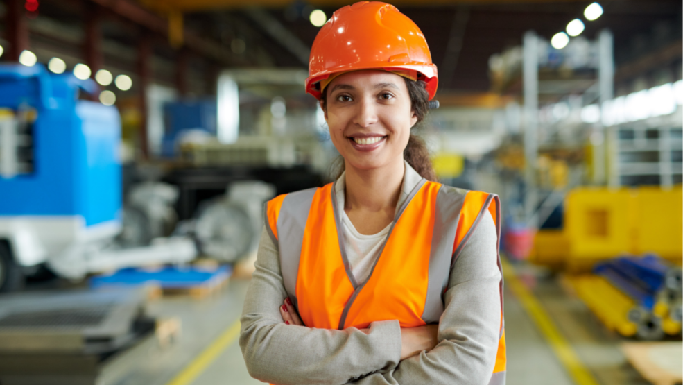 Woman working in warehouse setting wearing an orange safety helmet
