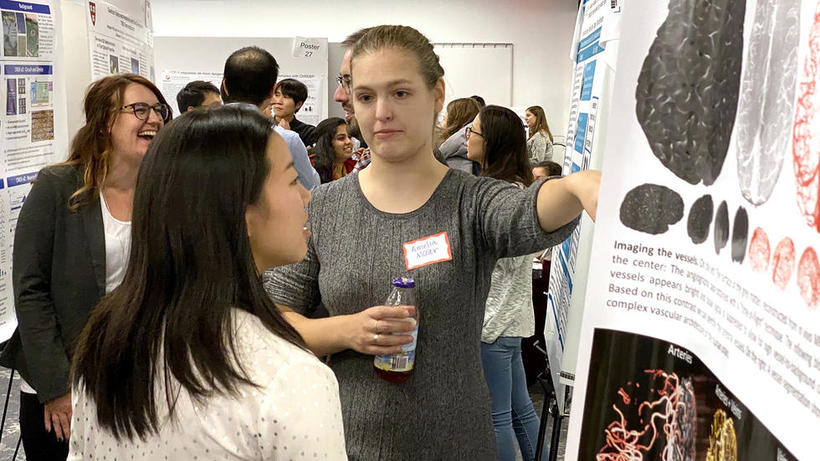 People stand in front of poster and discuss lab at HUROS Fair 2019