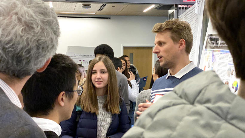 Group of students gather around lab representative and poster at HUROS 2019 fair
