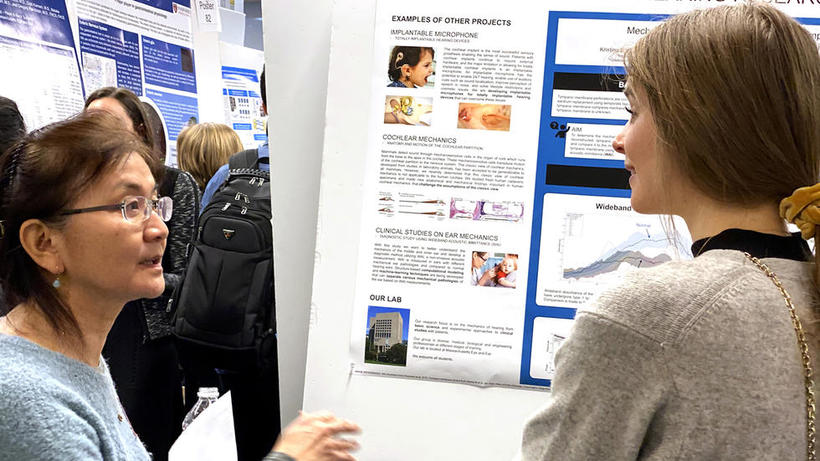 Female lab representative for hearing research discusses poster with female student at HUROS 2019 fair