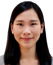 A young woman with straight black hair slightly past her shoulders, wearing a gray t-shirt, smiles at the camera in front of a white background.